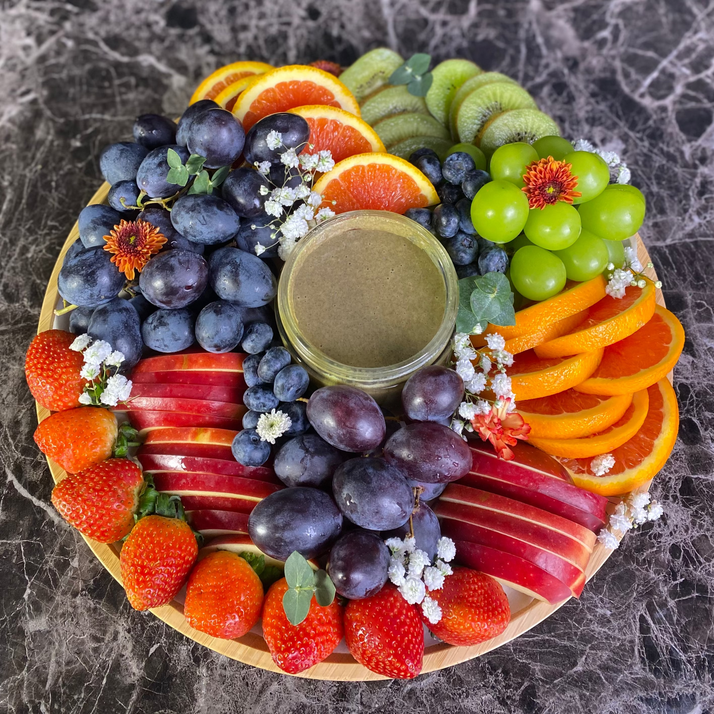 NuttaNut Pumpkin Seed Butter with fruit platter. fruit platter with a variety of fruits on a dark marble surface