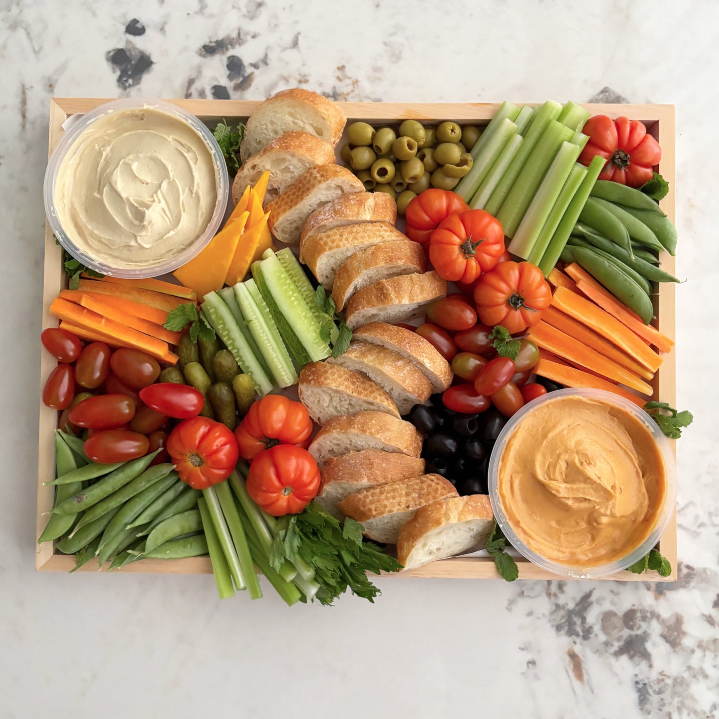 Platter of assorted vegetables, bread, and two types of dip on a marble surface. Le Bliss Platter’s Double Hummus Crudités Platter — a fresh vegetable platter with double hummus dips, available in Jakarta & Surabaya.