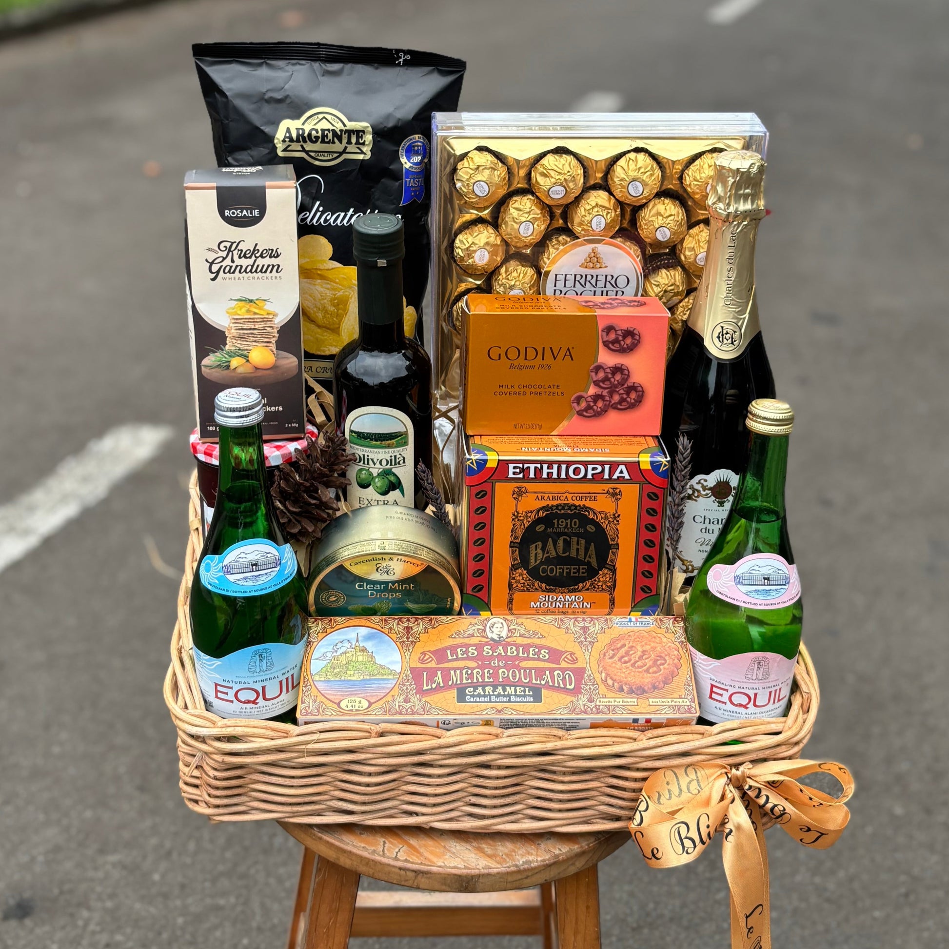Wicker basket with snacks, drinks, and chocolates on a stool in an urban street setting. hamper jakarta, hamper surabaya, gourmet hamper jakarta