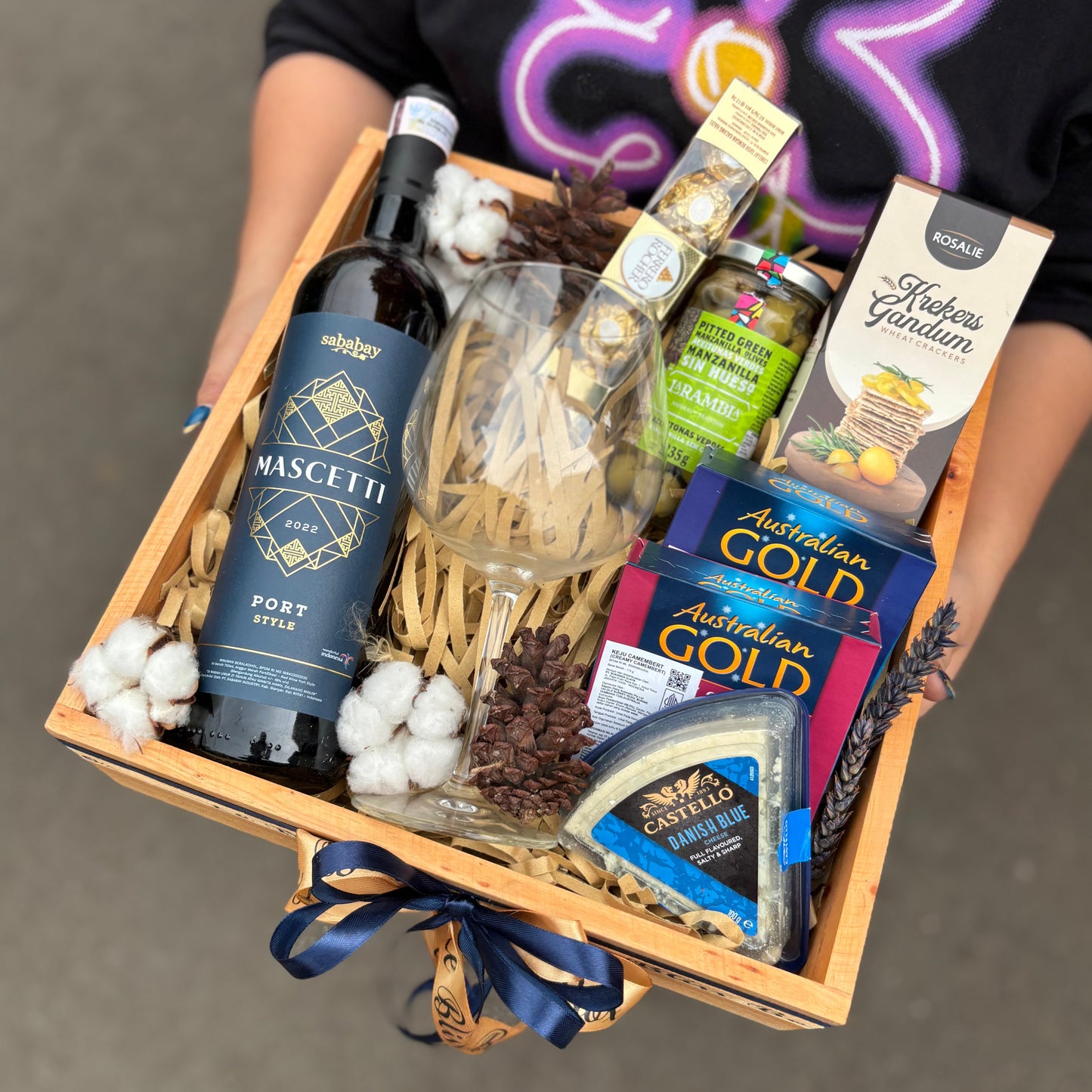 Wine Hamper Jakarta, Surabaya. Gift basket with wine, cheese, and other snacks on a dark surface. By Le Bliss Box