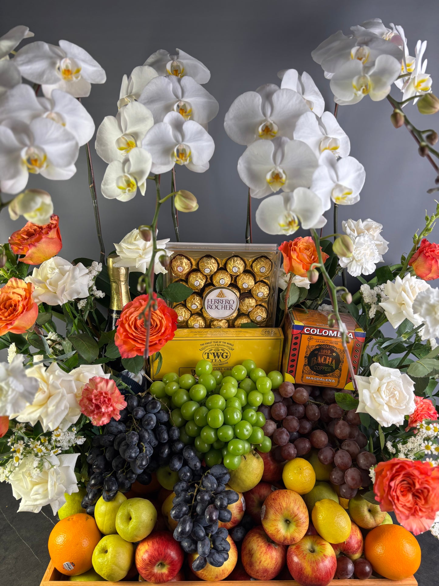 Wine hamper jakarta, Fruit and flower arrangement with chocolates and bacha twg tea on a dark background