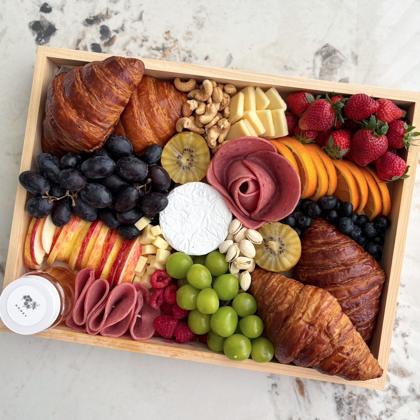 Wooden box filled with assorted fruits, cheeses, and pastries on a marble surface. Brunch Croissant Cheese Platter | Best Cheese Platter in Jakarta & Surabaya – Le Bliss Platter