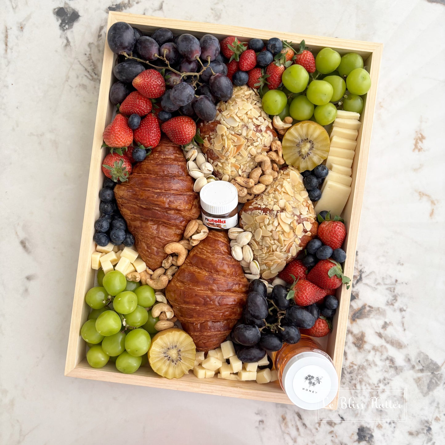 Wooden box filled with fruits, cheeses, and pastries on a marble surface. brunch platter jakarta, brunch platter surabaya, cheese platter jakarta. the best cheese platter and grazing service in jakarta by le bliss platter