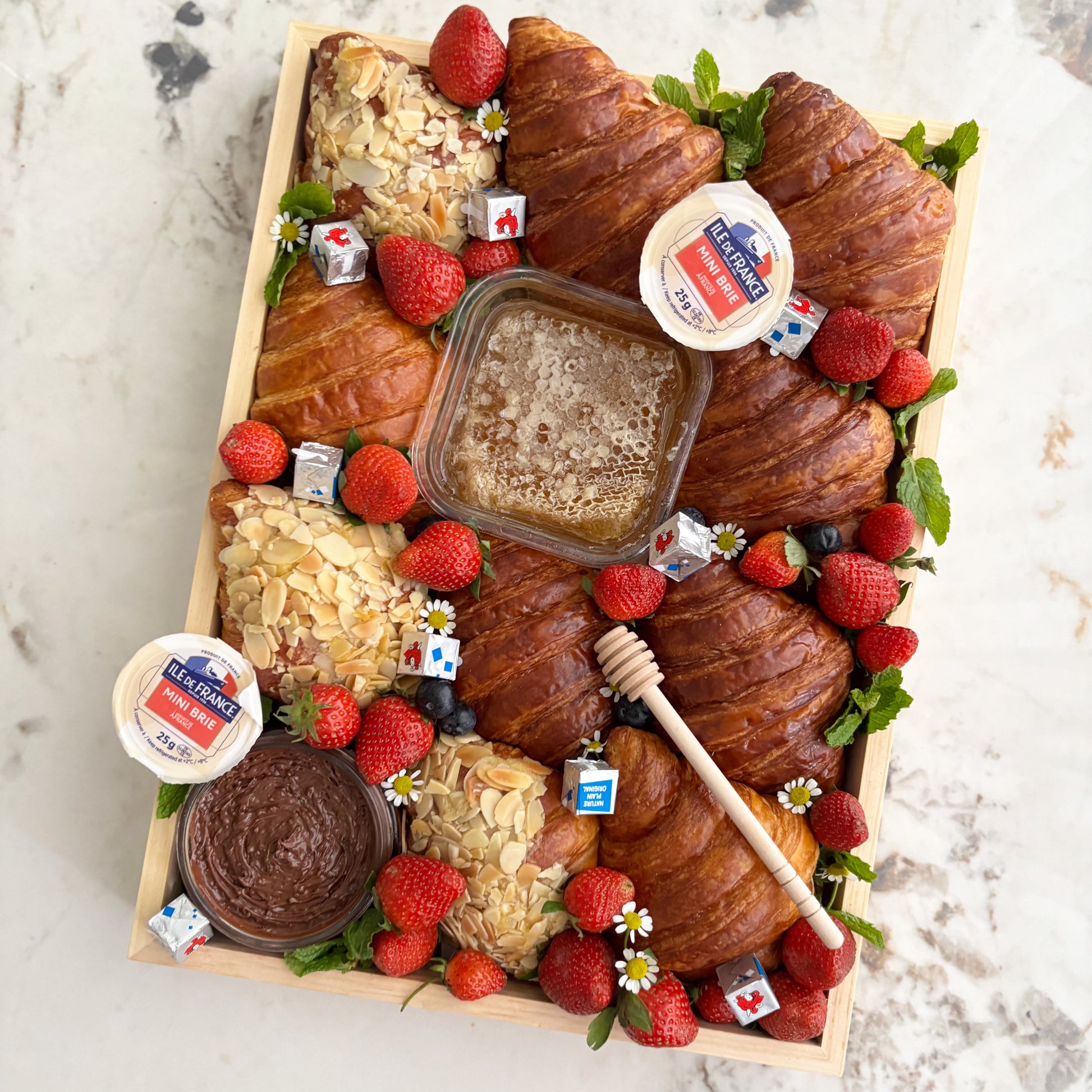 Wooden box of croissants with various toppings on a marble surface. Croissant Platter with cheese honey, cheese platter jakarta, cheese platter surabaya