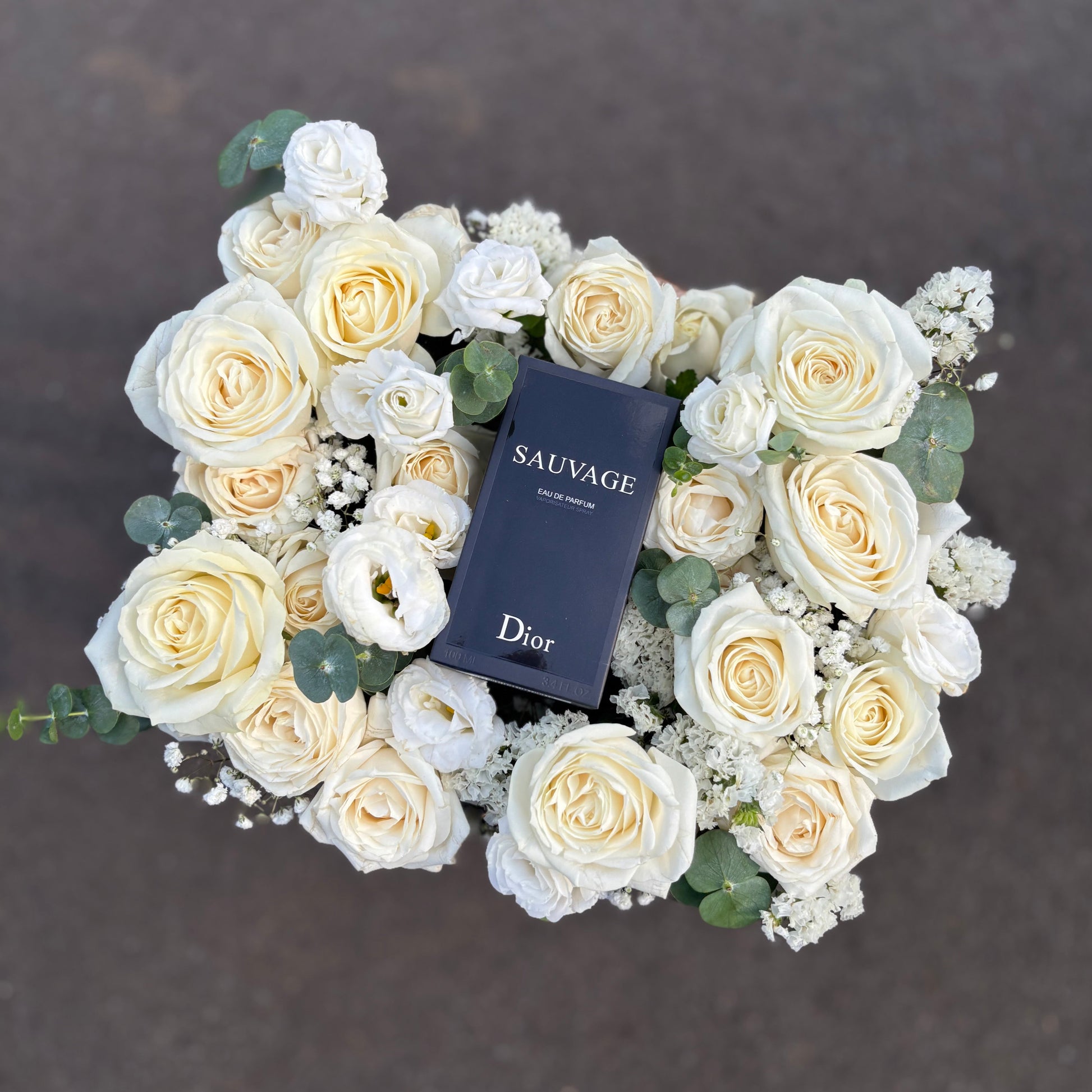 box of white roses with a Dior 'Sauvage' perfume bottle in the center on a dark background. perfume hamper jakarta