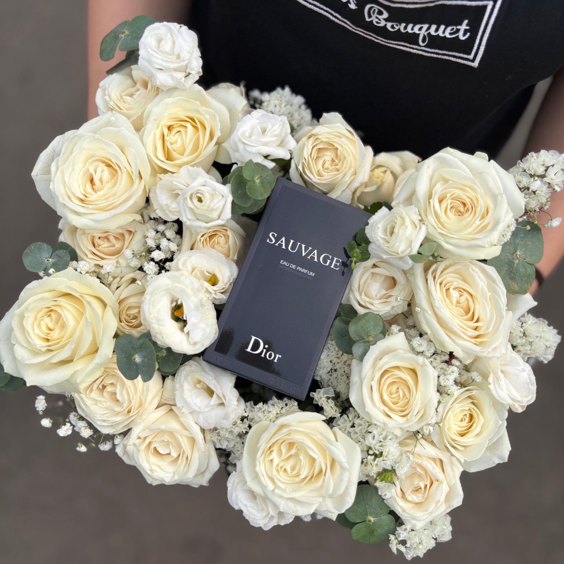 box of white roses with a Dior 'Sauvage' perfume bottle in the center on a dark background. perfume hamper jakarta, surabaya