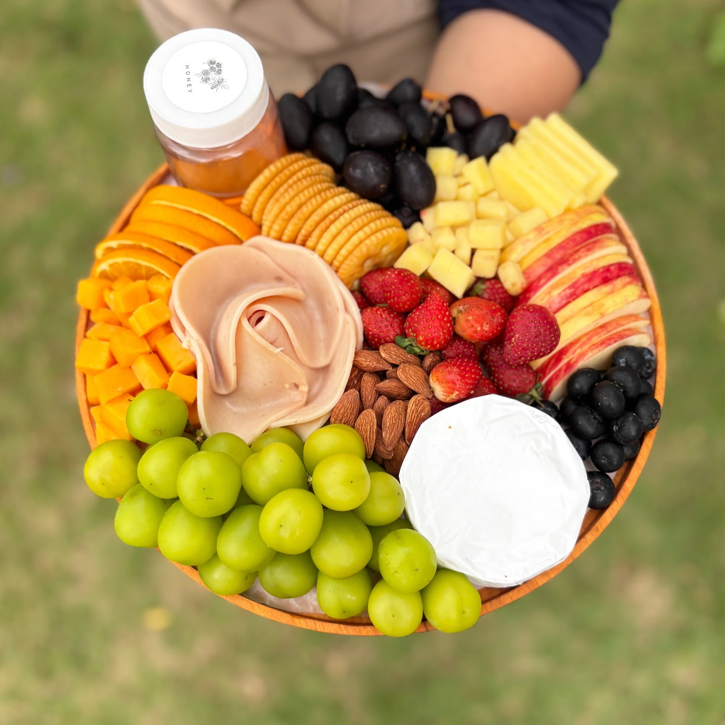chicken salami cheese platter. Assorted fruits, cheeses, and nuts on a platter with a blurred green background. best cheese platter in jakarta, surabaya. 