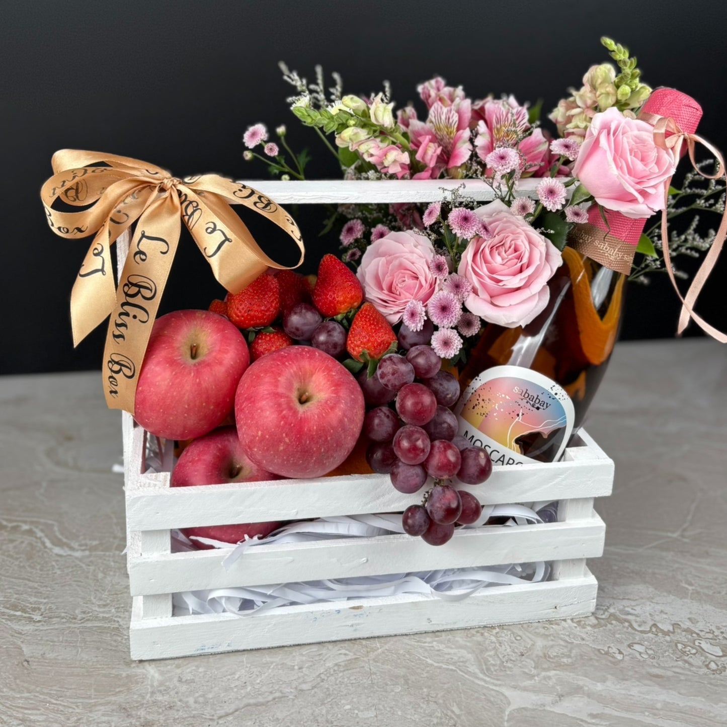 parcel buah dengan bunga dan wine. Gift basket with fruits, flowers, and a bottle of wine on a dark background. sababay wine hamper surabaya, jakarta, tangerang. fruit hamper with wine