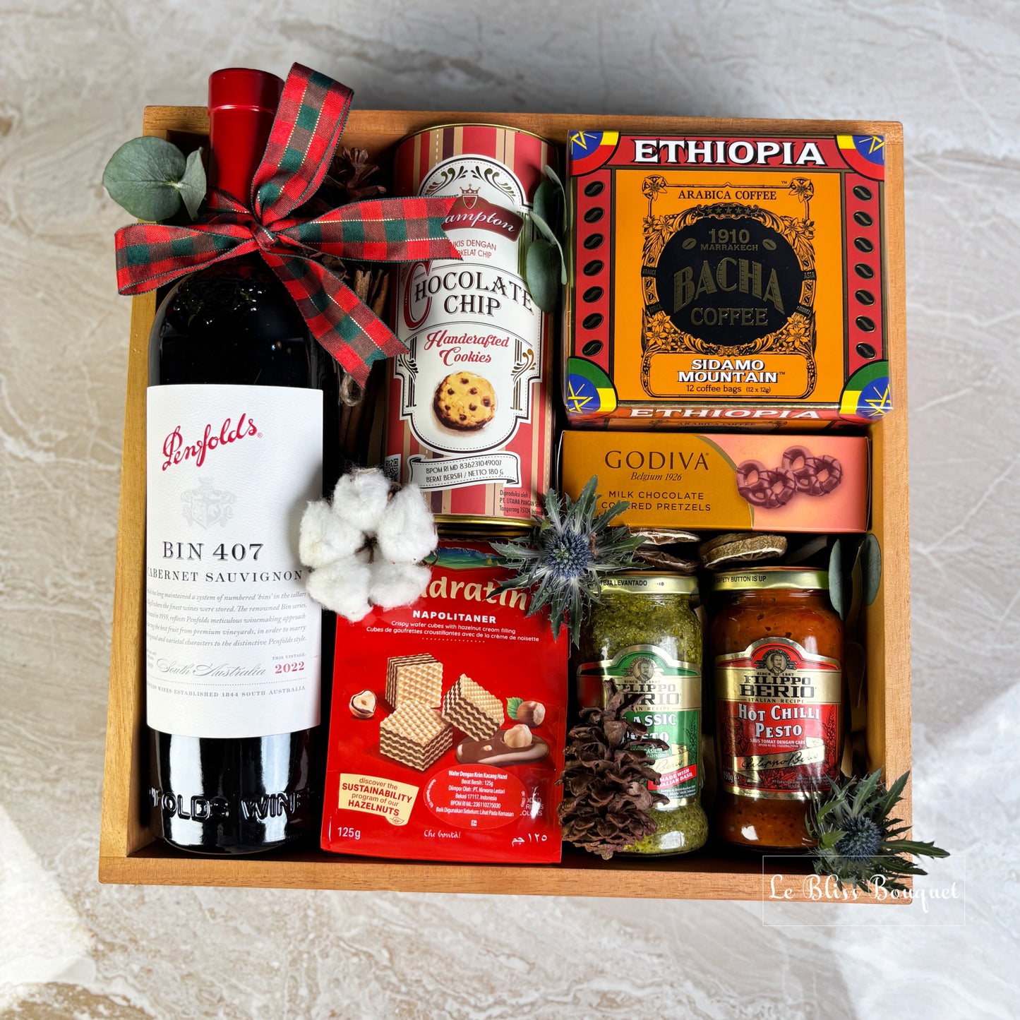 parcel with wine, cookies, and other snacks on a textured surface. hamper basket with wine, cookies, coffee, and snacks on a textured surface. wine bin 407 penfolds, bacha coffee and other. gourmet hamper jakarta, surabaya. parcel natal jakarta, parcel natal surabaya