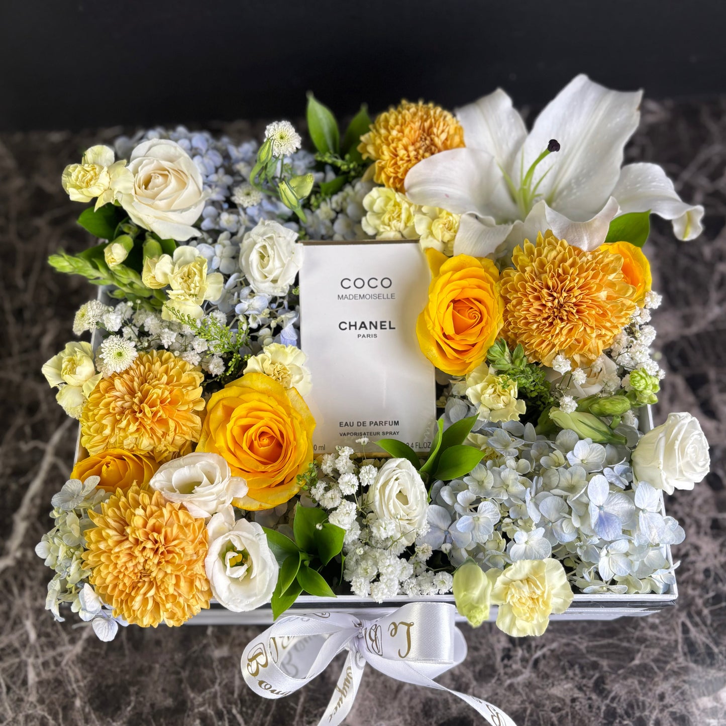 perfume hamper. Floral arrangement with a Chanel perfume bottle at the center on a marble surface. Perfume hamper jakarta, surabaya by le bliss bouquet