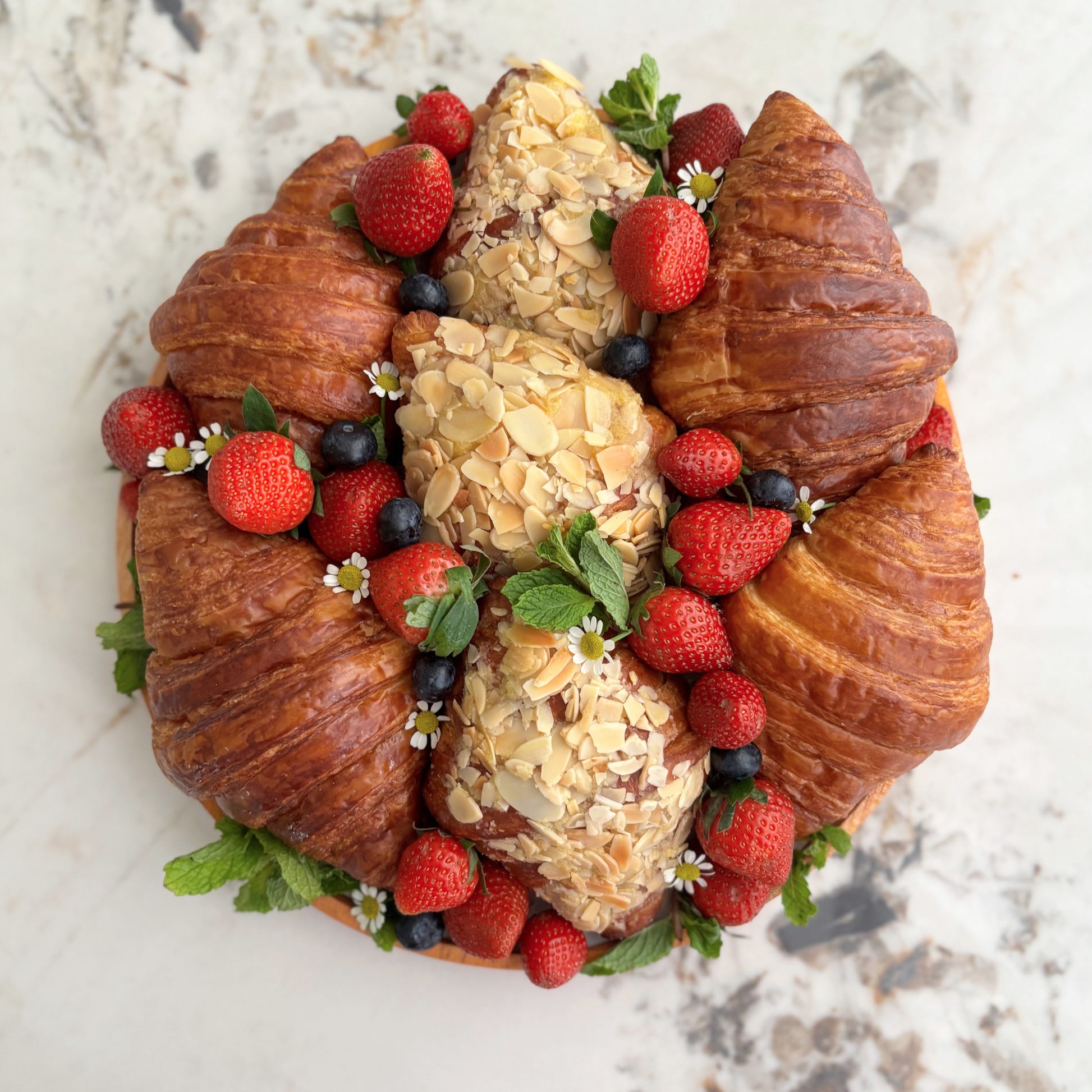 Decorative wreath made of croissants, almonds, and berries on a marble surface. Croissant platter with berries, buttery croissants, fresh berries & cream. The best sweet platter in Jakarta & Surabaya.
