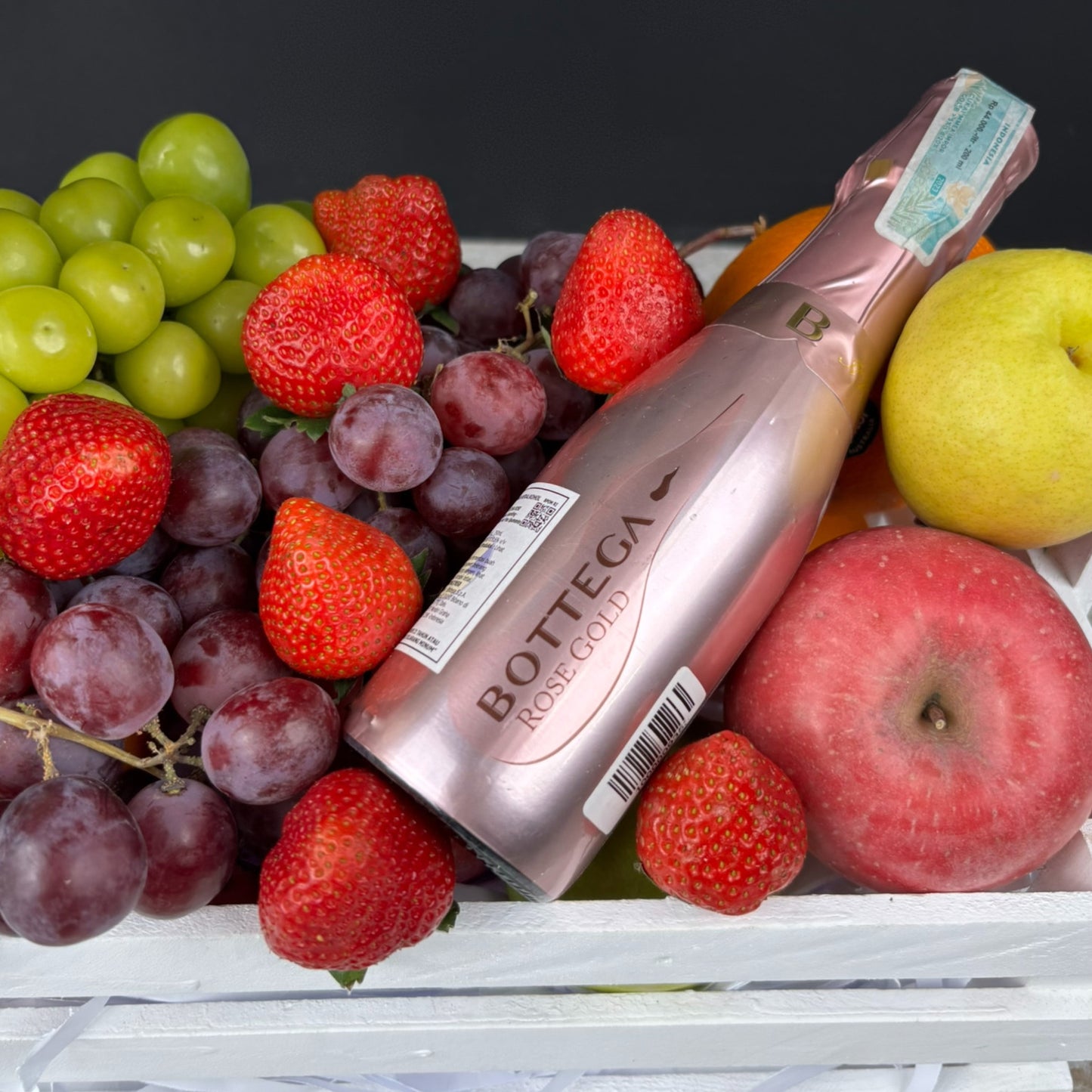 Bottle of Bottega Rose Gold champagne surrounded by fruits including grapes, strawberries, and apples on a dark background.