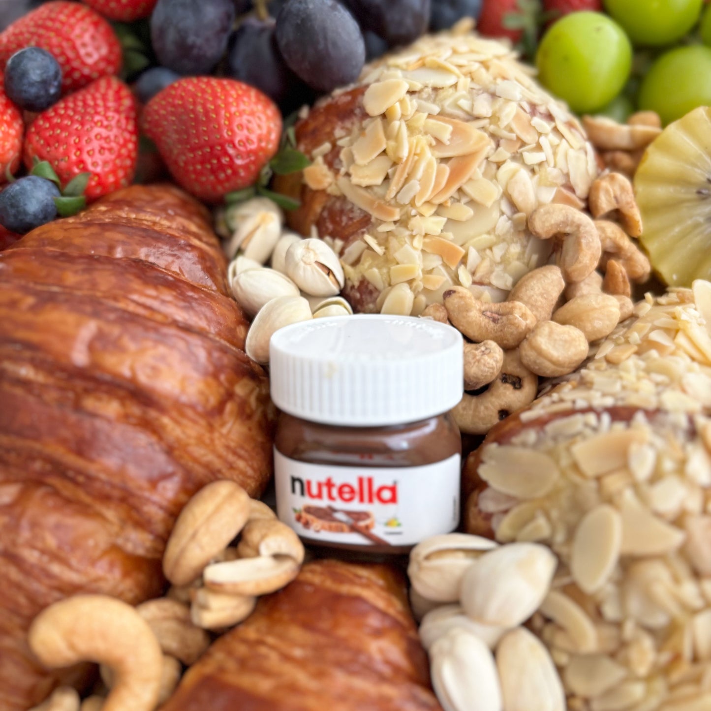 Nutella jar surrounded by assorted fruits and pastries