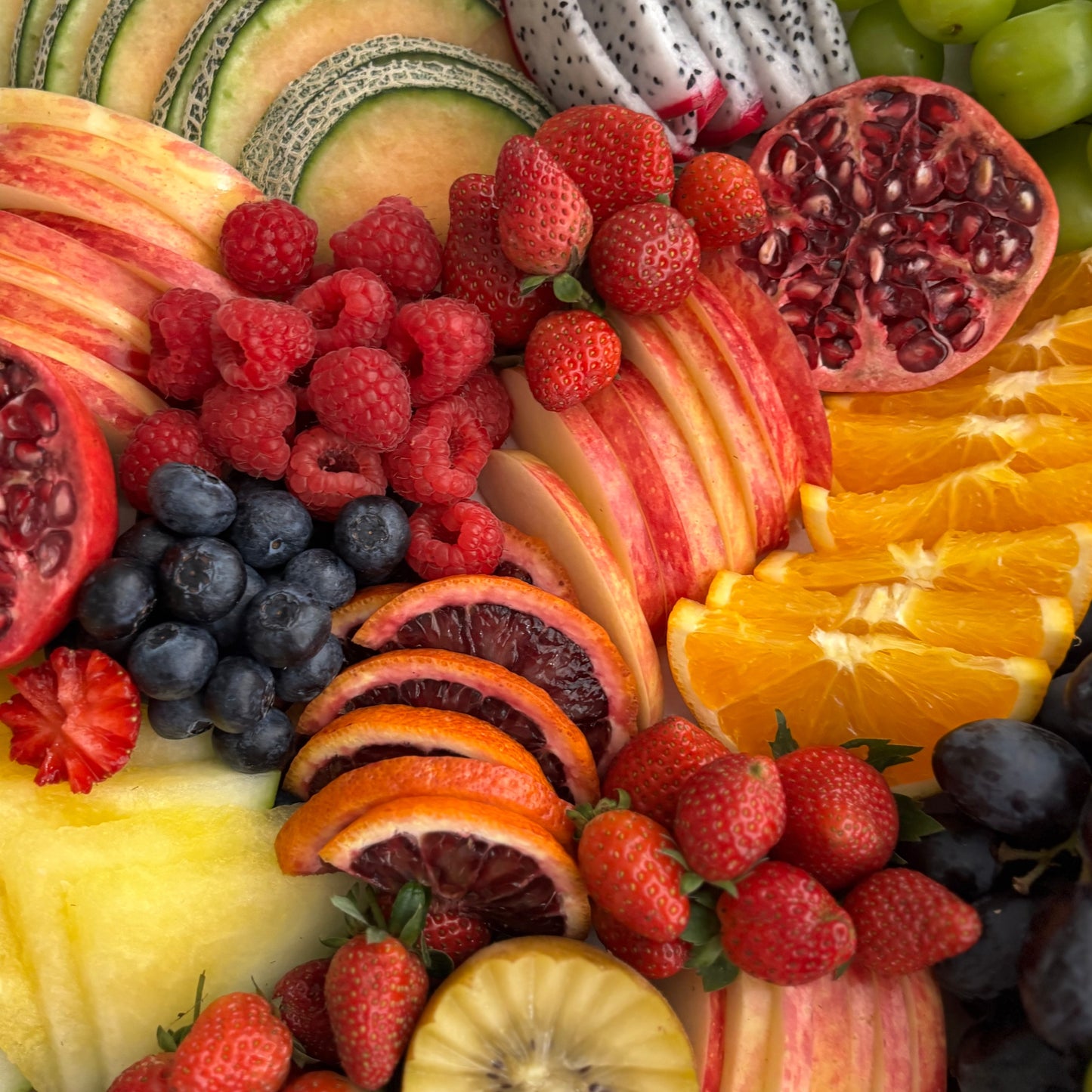 Assorted fruits including apples, oranges, strawberries, and grapes arranged on a plate.