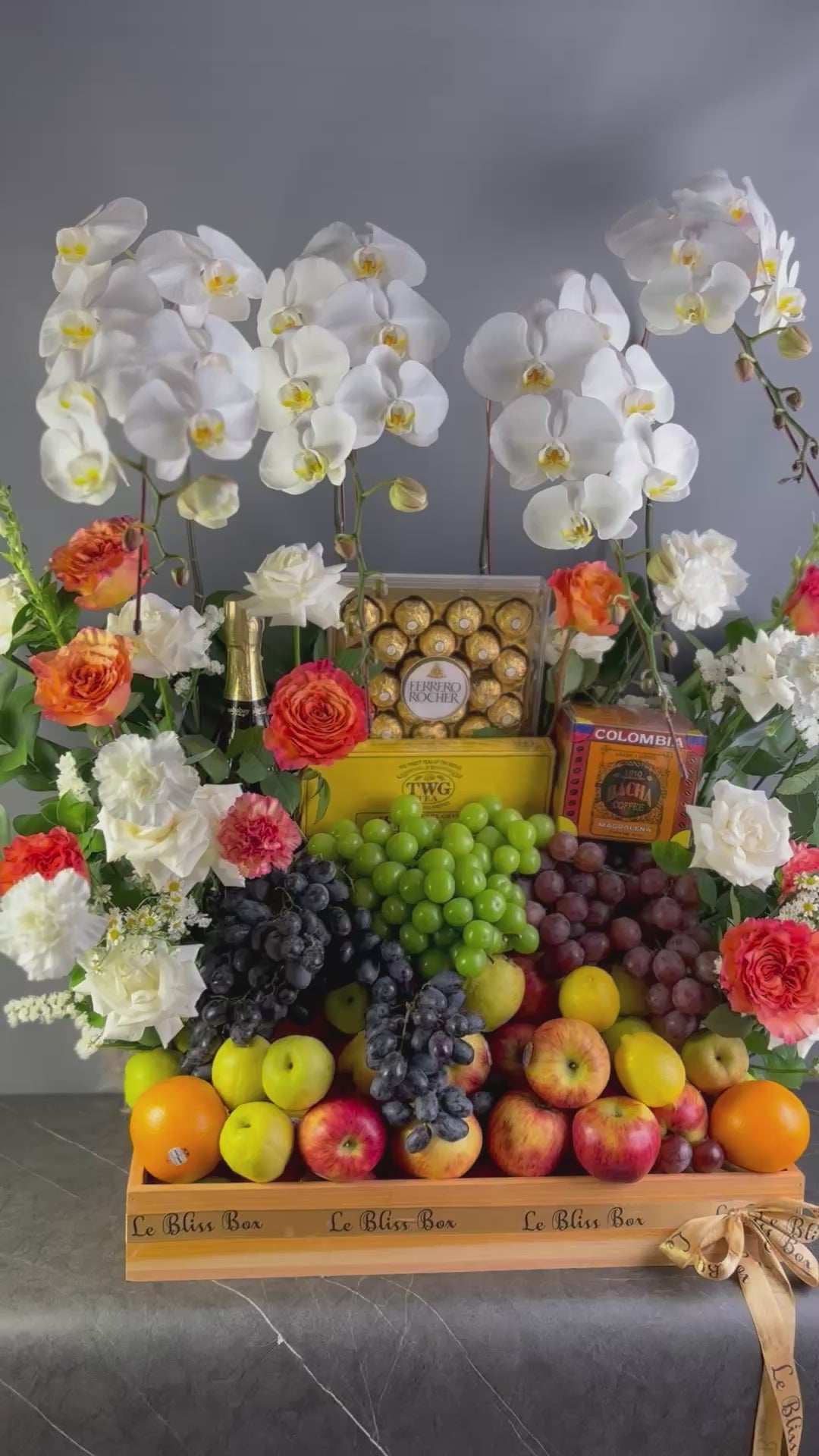 Fruit and flower arrangement with chocolates on a wooden stand against a gray background. luxury fruit hamper jakarta with wine. wine hamper surabaya & jakarta
