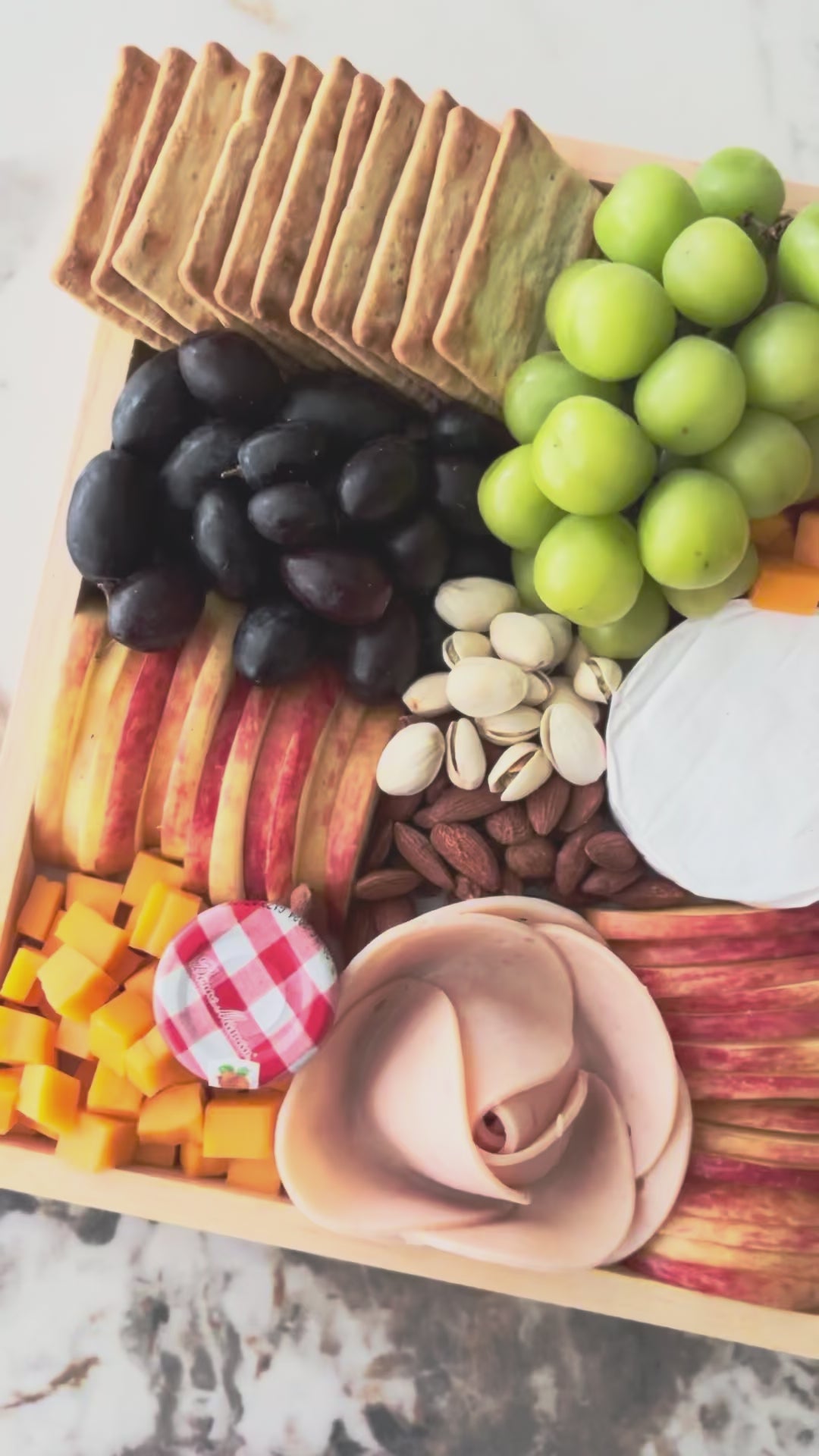 Assorted fruits, cheeses, and crackers on a wooden tray with a marble background, chicken salami, chicken pastrami, cheese platter jakarta, cheese platter surabaya