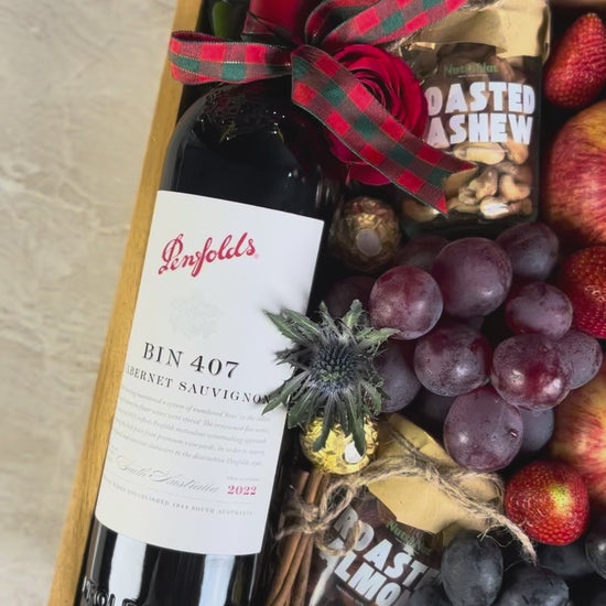 Gift box with Penfolds wine, fruits, and chocolates on a light background. Wine Hamper Jakarta by Le Bliss Box with roasted almond and cashew nuttanut. Penfolds Wine BIN 407 Hamper Jakarta