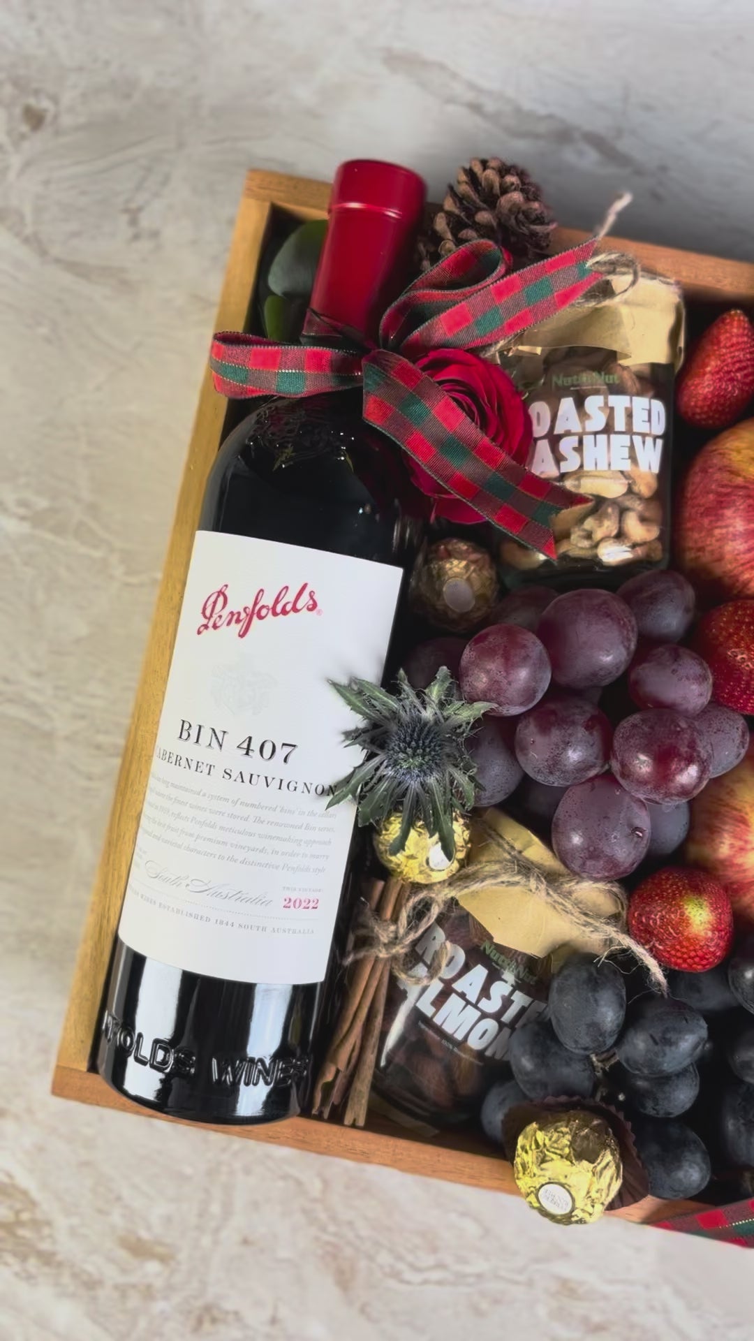 Gift box with Penfolds wine, fruits, and chocolates on a light background. Wine Hamper Jakarta by Le Bliss Box with roasted almond and cashew nuttanut. Penfolds Wine BIN 407 Hamper Jakarta