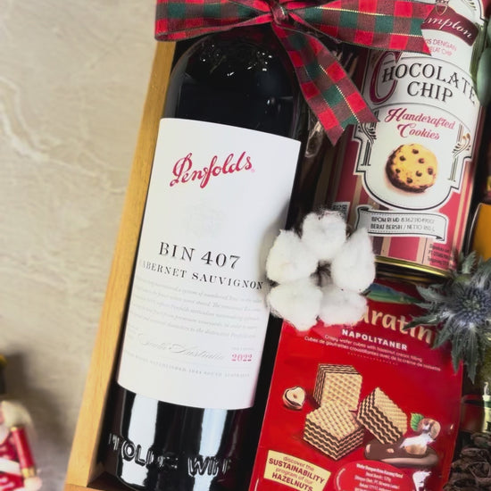 Gift basket with wine, cookies, coffee, and snacks on a textured surface. wine bin 407 penfolds, bacha coffee and other. gourmet hamper jakarta, surabaya. parcel natal jakarta, parcel natal surabaya