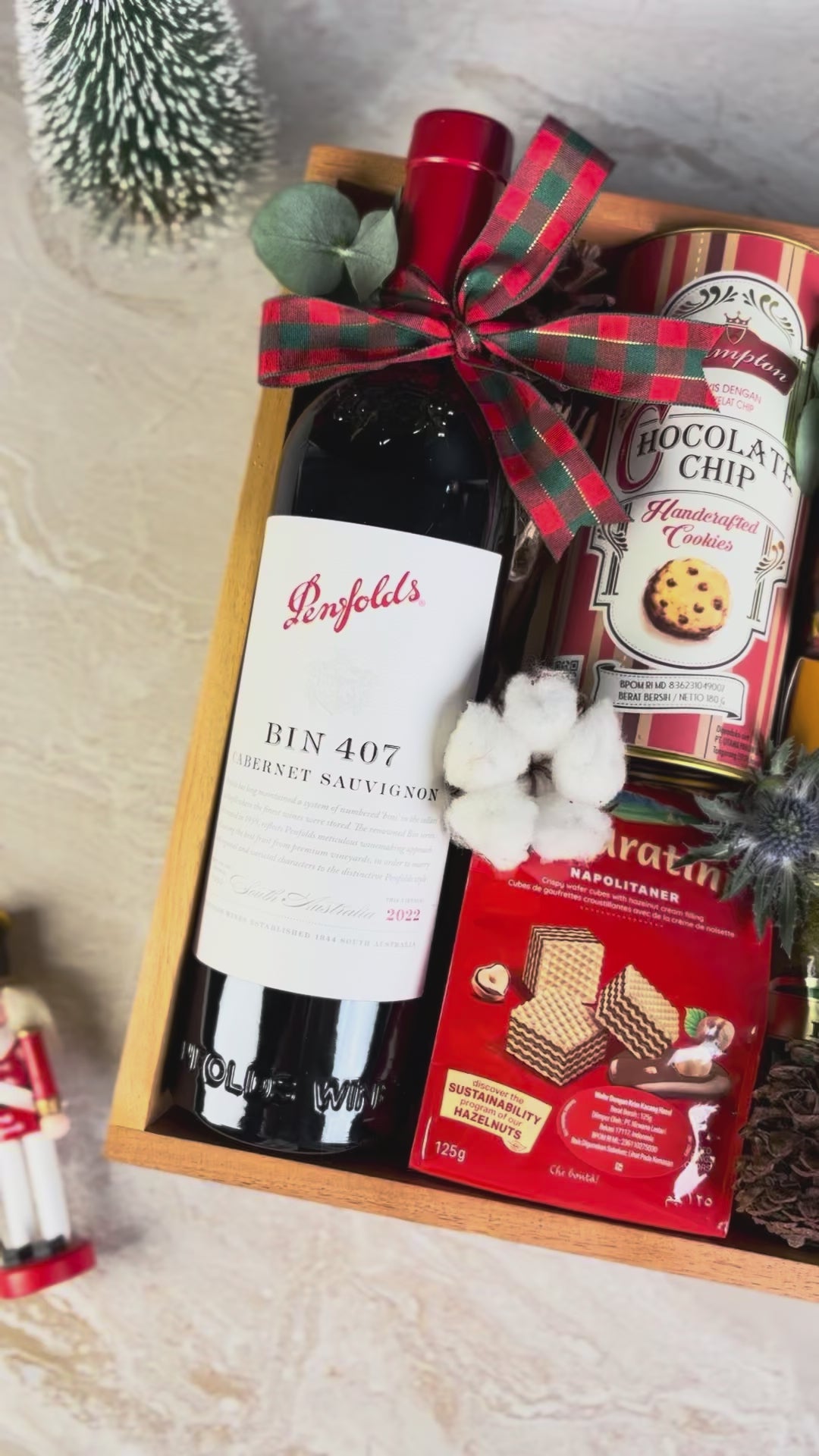 Gift basket with wine, cookies, coffee, and snacks on a textured surface. wine bin 407 penfolds, bacha coffee and other. gourmet hamper jakarta, surabaya. parcel natal jakarta, parcel natal surabaya