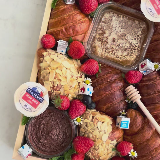 Assorted croissants with fruits and pastries on a marble surface. Wooden box of croissants with various toppings on a marble surface. Croissant Platter with cheese honey, cheese platter jakarta, cheese platter surabaya