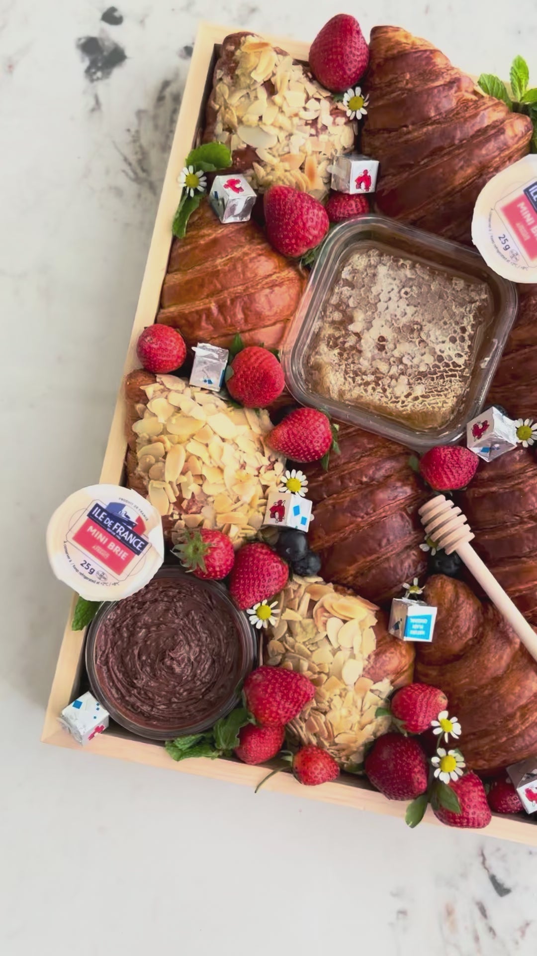 Assorted croissants with fruits and pastries on a marble surface. Wooden box of croissants with various toppings on a marble surface. Croissant Platter with cheese honey, cheese platter jakarta, cheese platter surabaya