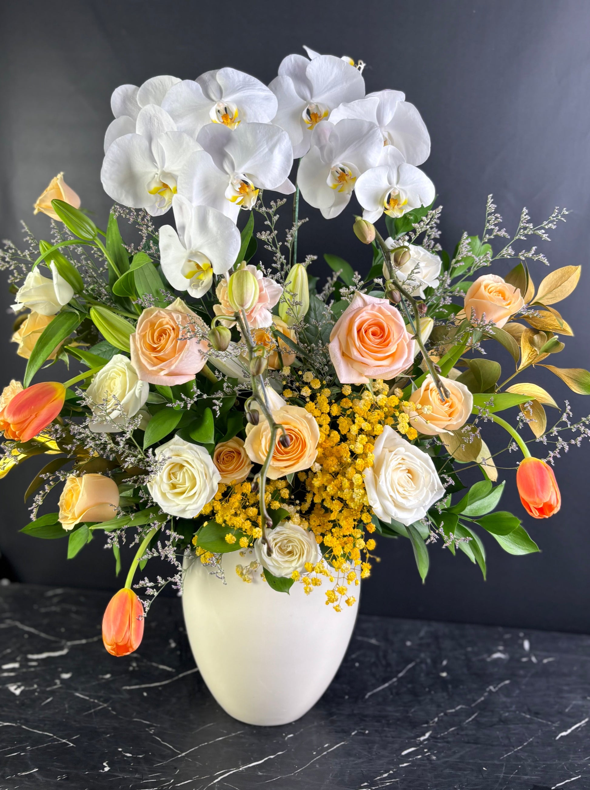 vase arrangement with white orchids, roses, and other flowers in a white vase on a dark surface. flowers with white orchids, roses, and other flowers in a vase on a dark surface. Florist Jakarta, Surabaya, Cirebon